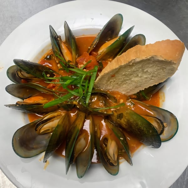 PK Oyster Bar's mussels in red sauce, garnished with green onions and a slice of bread.