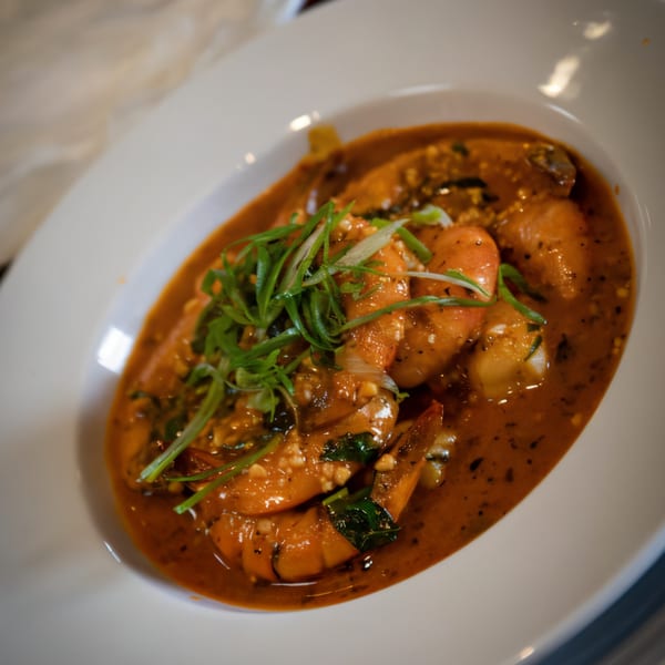 PK Oyster Bar's shrimp dish in a rich, reddish-brown sauce, garnished with fresh green onions.