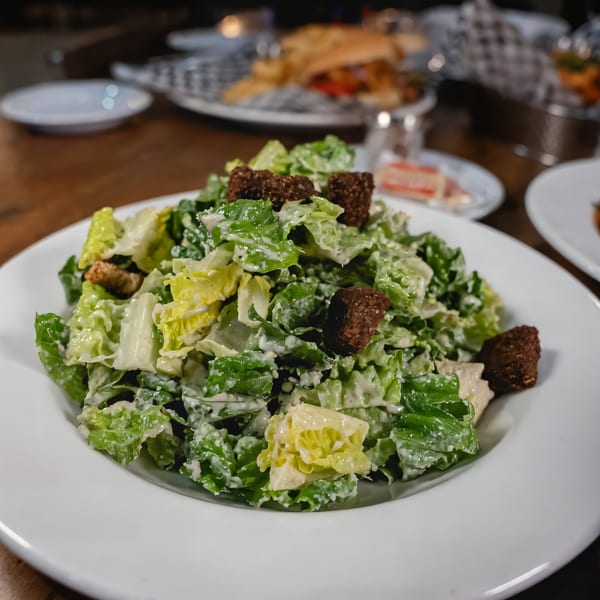 Fresh Caesar salad with crisp romaine lettuce, creamy dressing, and dark croutons on a white plate.