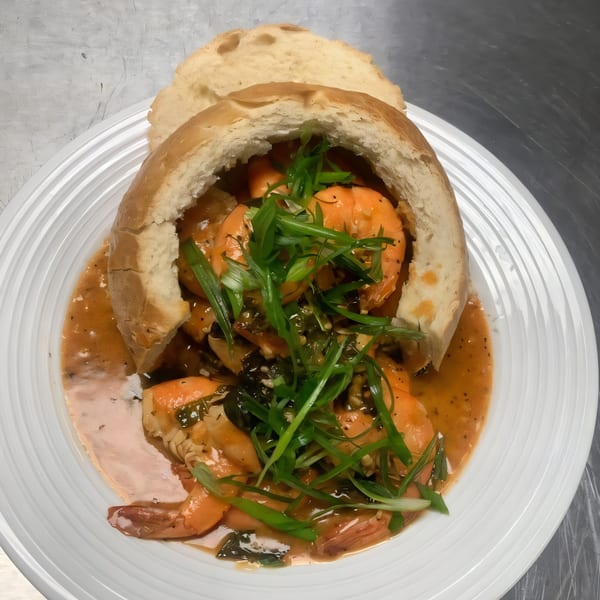 Shrimp scampi in a bread bowl, garnished with green onions, on a white plate.