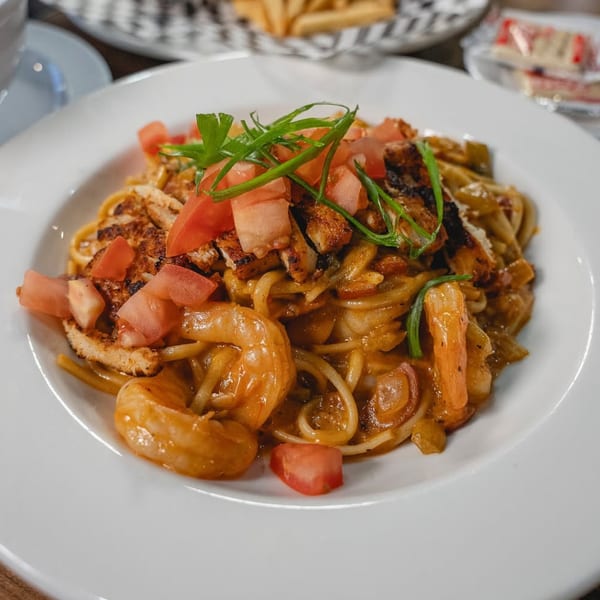 PK Oyster Bar's seafood pasta with shrimp, chicken, tomatoes, and green onions on a white plate.